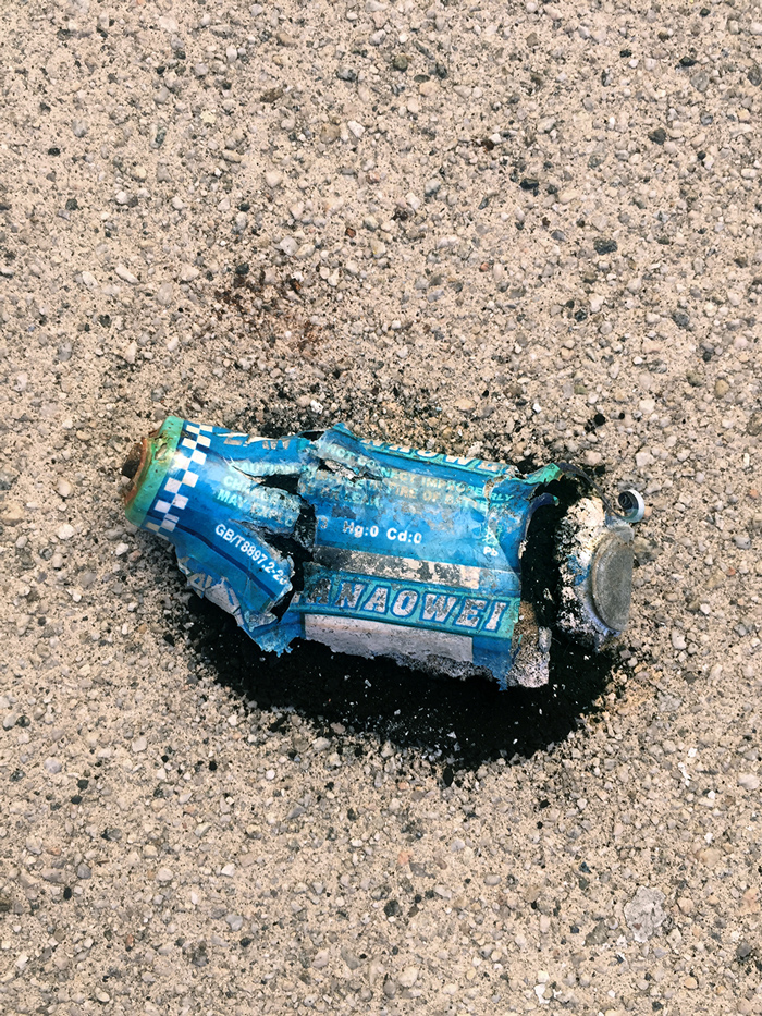 broken blue AA battery with black powder spilling out, on concrete