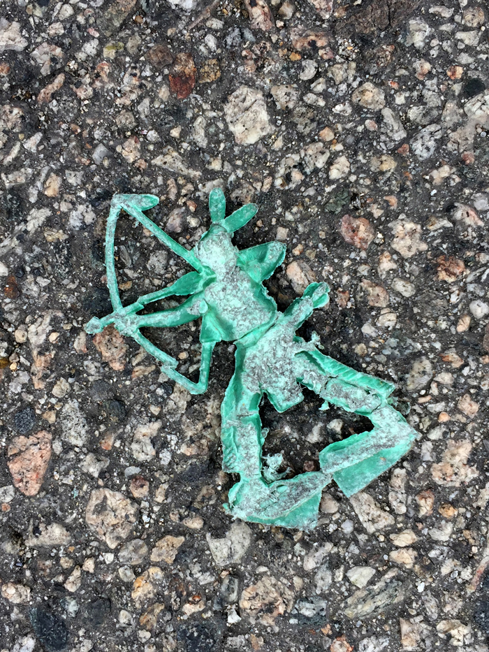 smashed green toy shaped like native american with bow, in the street