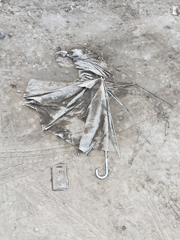 mangled umbrella and plastic pouch embedded in dirt on the ground