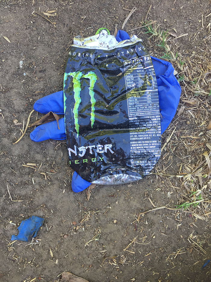 crushed can of Monster Energy Drink over a blue latex glove
